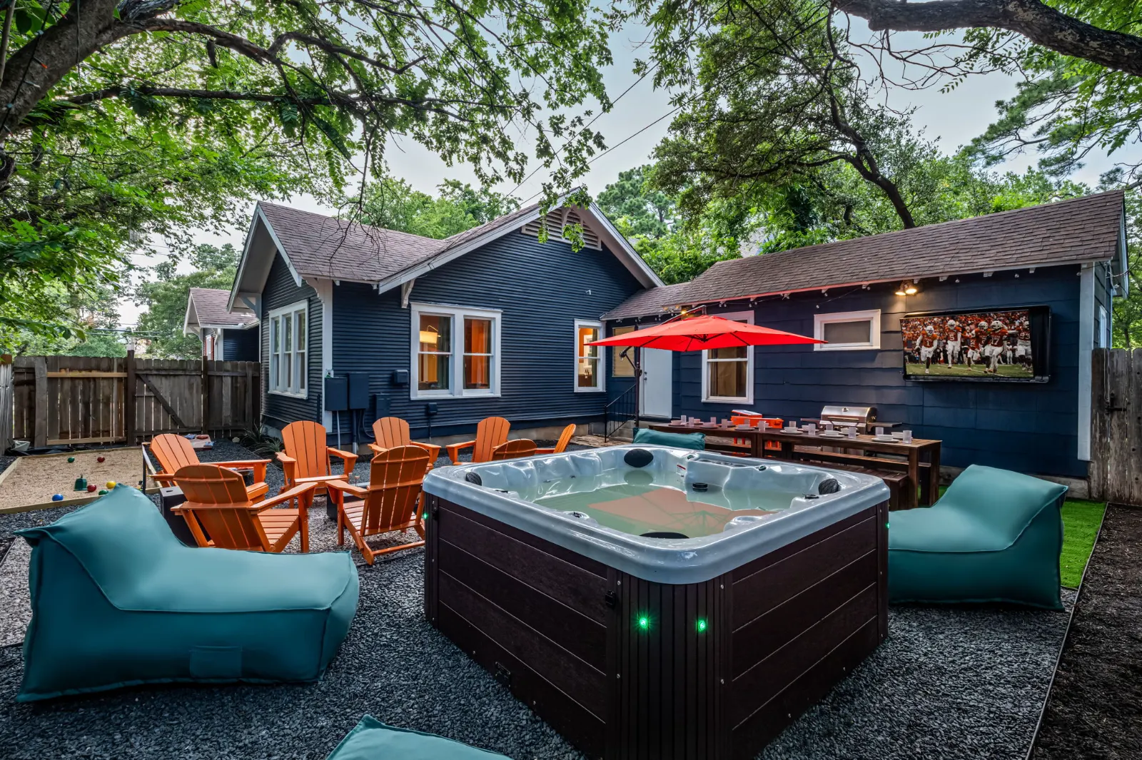 After the buildout: the same bungalow painted navy, with a hot tub, loungers, Adirondack chairs around a fire pit and an outdoor TV