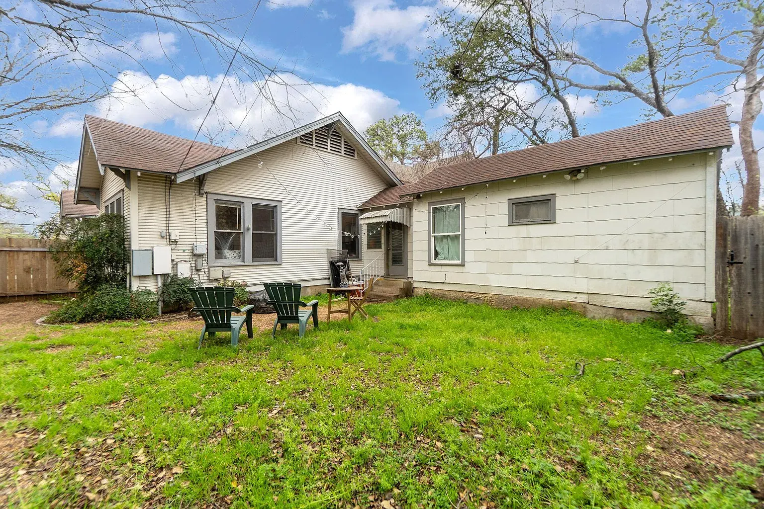 Before the buildout: a plain white bungalow with a patchy lawn and two lawn chairs
