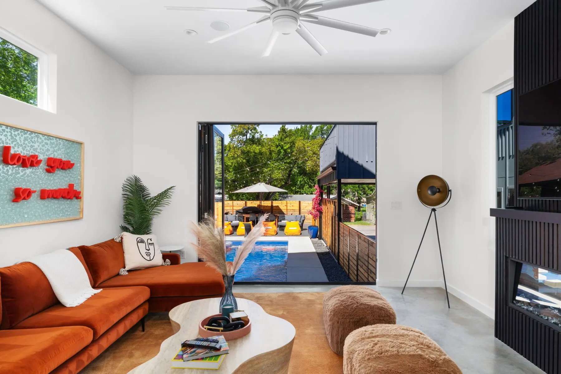 ArtHaus: a white living room with a rust sectional and a neon sign, opening onto the pool