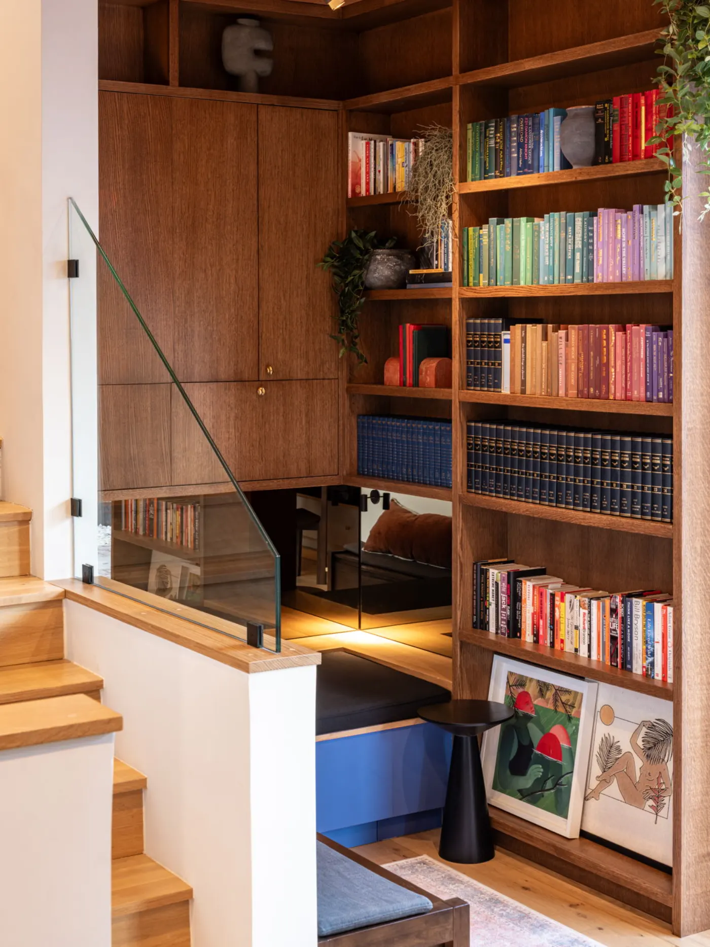 Built-in wooden bookshelves beside a short flight of stairs, with a glass balustrade and a reading nook below