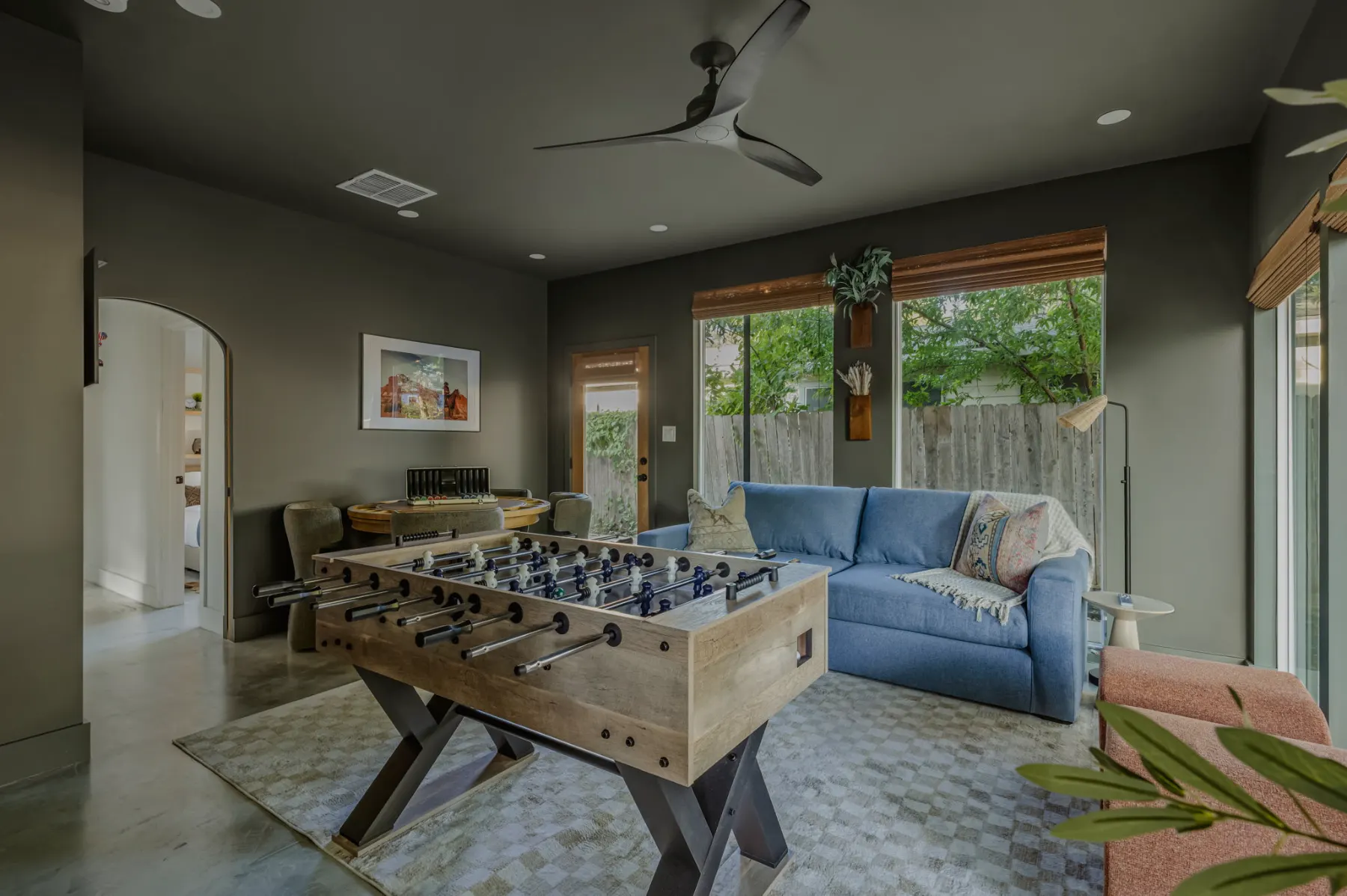 A game room with a foosball table, a blue sofa and arched doorways, lit by tall windows