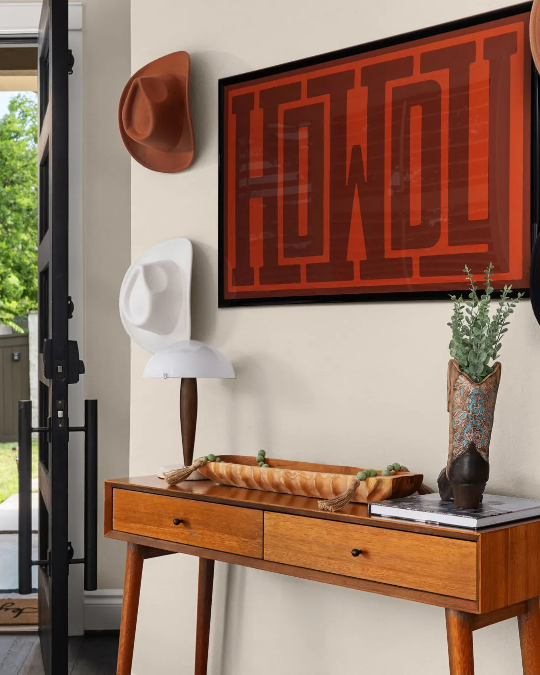 An entry console with a cowboy hat on a hook and a red "Howdy" sign above a mid-century wooden table