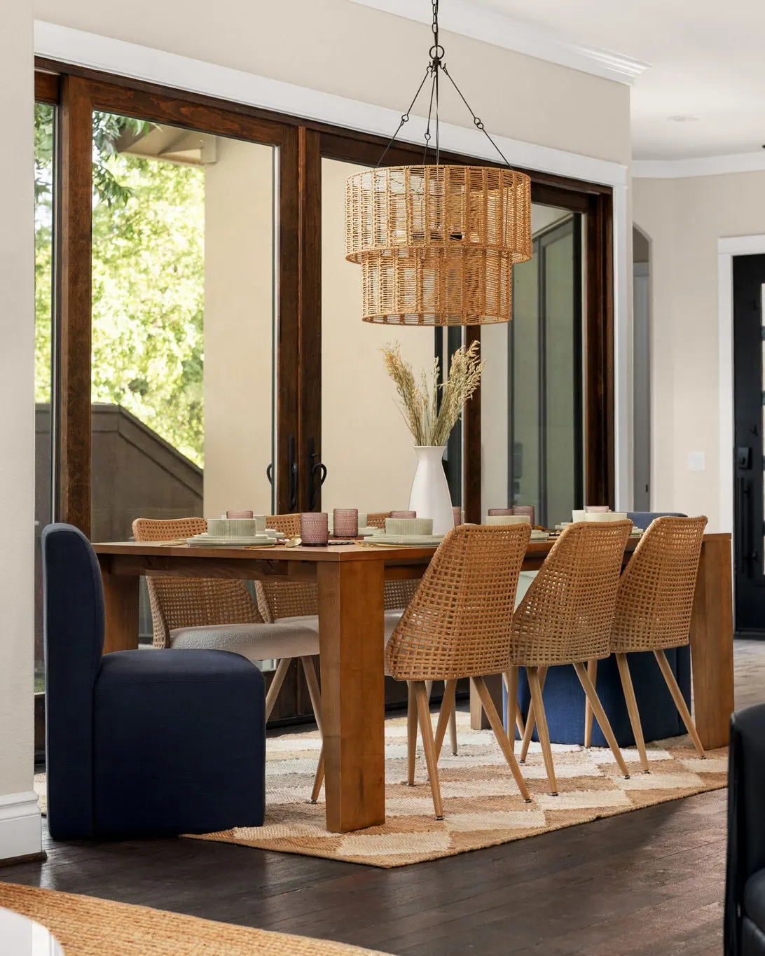 A dining table with rattan chairs under a woven pendant light, beside sliding doors to the garden