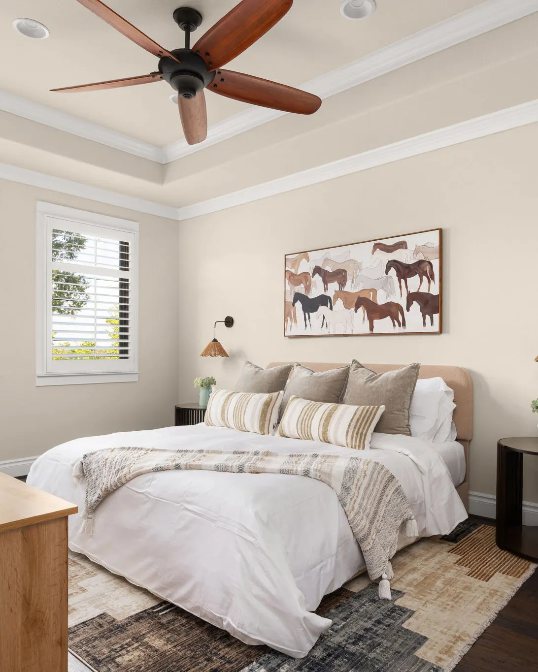 A bedroom with a white bed, a western horse print above the headboard and a ceiling fan