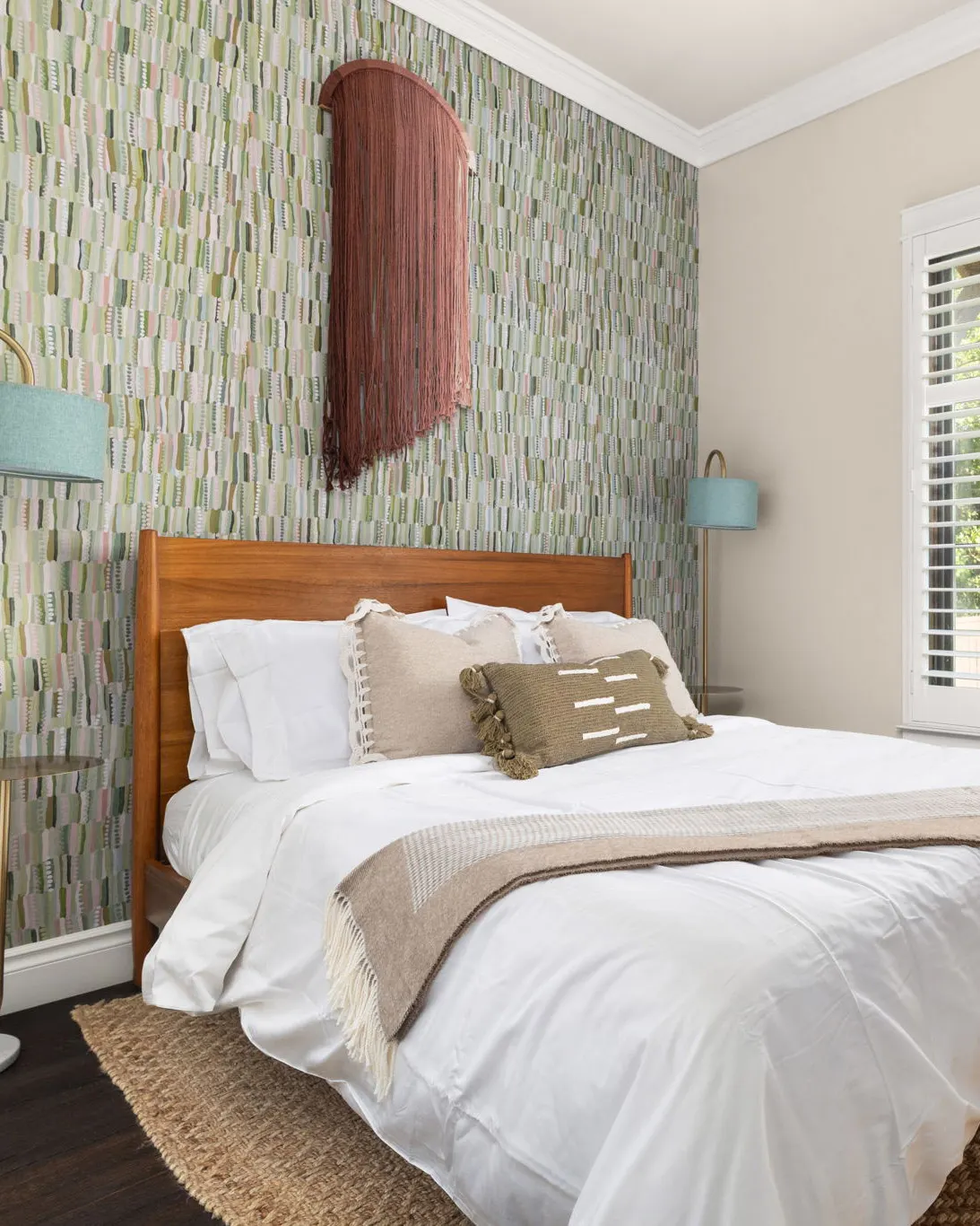 A bedroom with a green tiled feature wall behind a wooden headboard and a rust-colored wall hanging