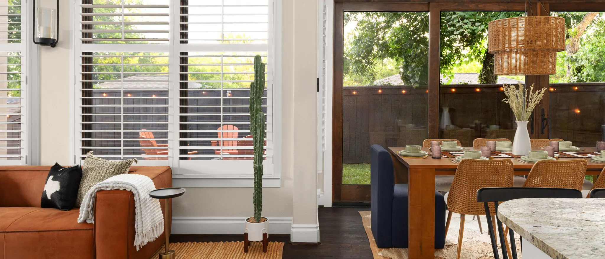 The living room opening onto the dining area, with a potted cactus, a leather sofa and a woven pendant light