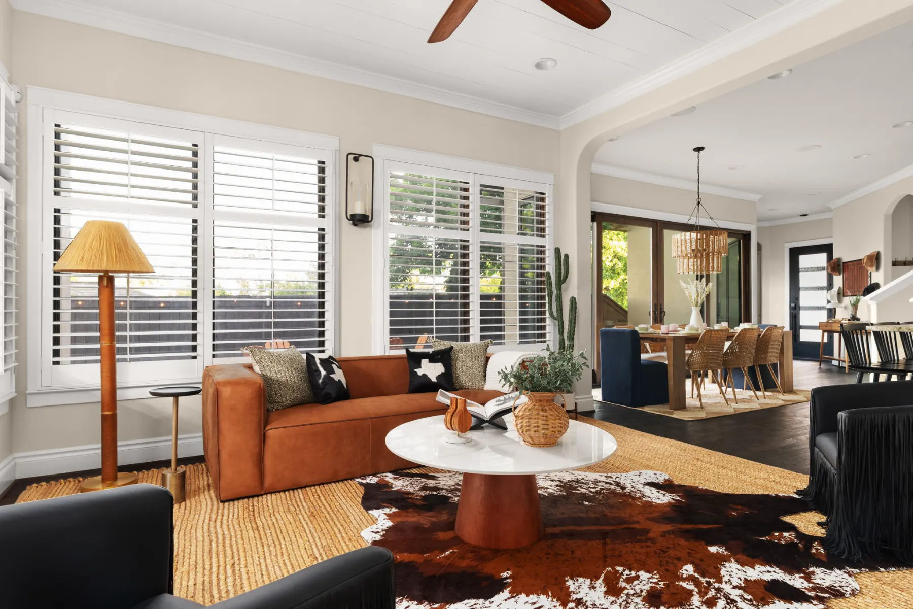 The living room after the redesign: a cognac leather sofa, a round white coffee table on a cowhide rug, and the dining area beyond